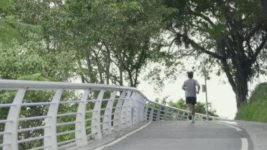 Parkta koşan Asyalı bir gencin arka görüntüsü.