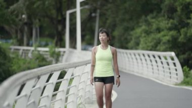 young asian jogger walking resting in park while exercising outdoors