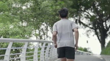 rear view of young asian man jogger male athlete jogging running exercising training outdoor in park