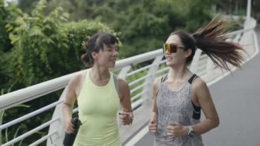 two happy young asian women joggers jogging running exercising outdoors in park