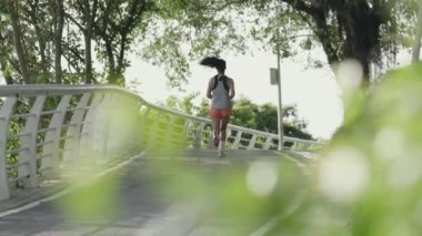 Parkta koşan Asyalı genç bir kadının arka görüntüsü.