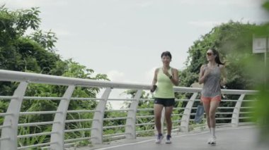 İki genç Asyalı bayan arkadaş parkta koşu yapıyorlar.
