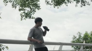 Genç Asyalı erkek sporcu. Açık hava egzersizi sırasında su içiyor.