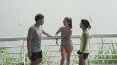 Üç genç Asyalı dışarıda egzersiz yaparken sohbet ediyorlar.