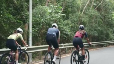 Kırsal yolda bisiklet süren üç genç Asyalı bisikletçinin arka görüntüsü