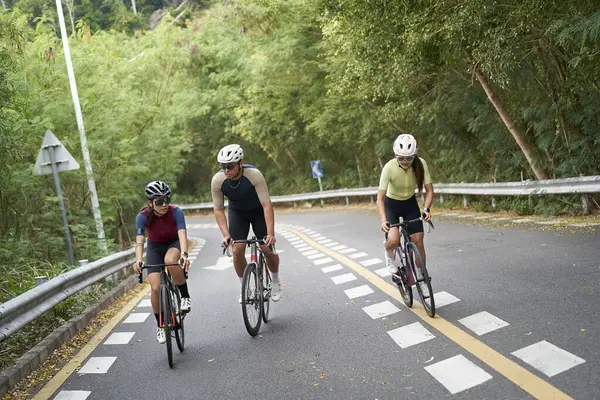 三位年轻的亚洲骑单车人士在乡间路上骑单车 图库照片