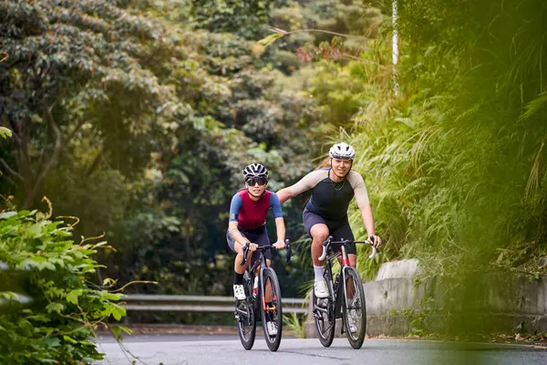 年轻的亚洲夫妇骑自行车在乡间路上 免版税图库图片