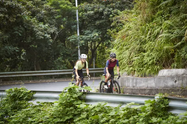 田舎の道路で自転車に乗る2人の若いアジアの女性サイクリスト ストック写真