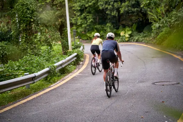 田舎の道路で自転車に乗っている若いアジアのカップルサイクリストのリアビュー ロイヤリティフリーのストック画像