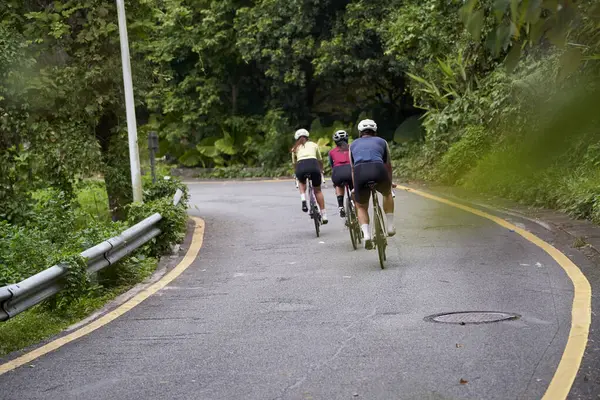 田舎の道路で自転車に乗っている3人の若いアジアのアダルトサイクリストのリアビュー ストックフォト
