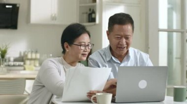 Masada oturan üst düzey Asyalı çift dizüstü bilgisayarla finansal planlar yapıyor.