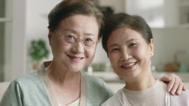 İki mutlu Asyalı kadının portresi. Kanepede oturmuş kameraya bakıp gülümsüyor.