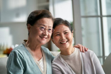 Evdeki kanepede oturmuş gülümseyen iki yaşlı Asyalı kadının portresi.