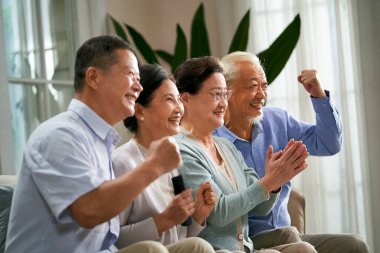 Bir grup mutlu Asyalı çift evde kanepede oturup spor maçı izliyorlar.