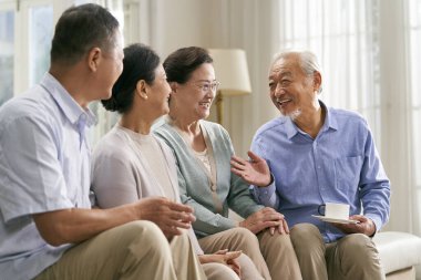 Bir grup mutlu kıdemli Asyalı evdeki kanepede oturup keyifli bir sohbet ediyorlar.