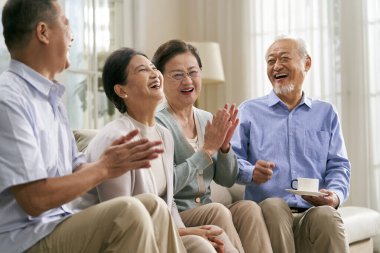 Bir grup mutlu kıdemli Asyalı evdeki kanepede oturup keyifli bir sohbet ediyorlar.