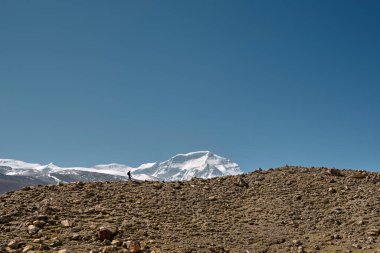 Sırt çantalı Asyalı fotoğrafçı arkadaki Cho oyu dağıyla mavi gökyüzünün altında dağ sırtında yürüyor.