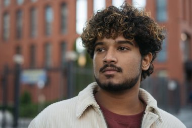 Dalgın, kıvırcık saçlı, şık ceketli, caddeye bakan Hintli adamın yakın plan portresi. 