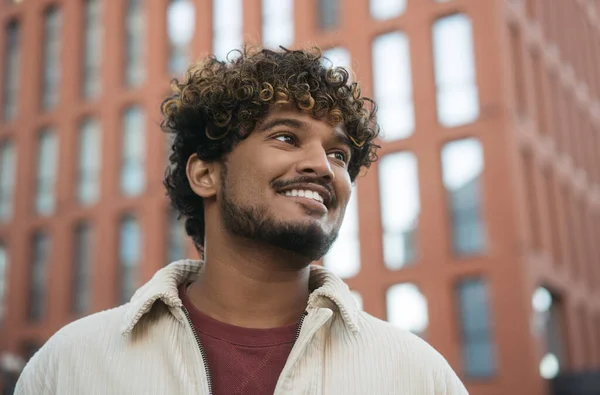 stock image Closeup portrait of smiling Indian man with stylish curly hair looking away on the street. Handsome asian fashion model wearing trendy jacket posing for picture outdoors, copy space  