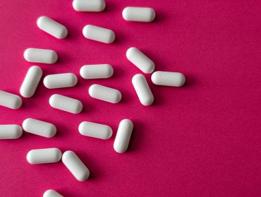 Pembe arka planda dağınık beyaz kapsüller