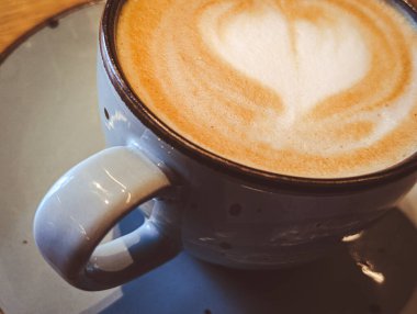İçi sıcak kapuçino dolu mavi bir seramik fincanın yakın çekimi. İçinde güzel latte sanatları var.