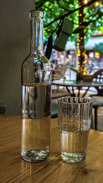 Temiz suyla dolu temiz bir cam şişe ve ahşap masaya yerleştirilmiş bir bardak.