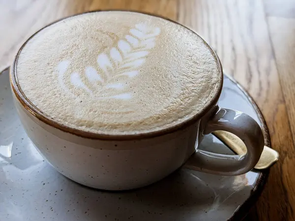 Bir kapuçinonun yakın plan fotoğrafı. Masada seramik bir fincanda latte resmi var.