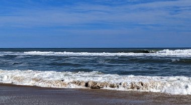 Dalgalar ve kumla aydınlık bir öğleden sonra mavi gökyüzü ve bulutlar - Assateague, MD, ABD