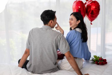 Back view of couple sitting on the bed, couple with red heart shape balloons Valentine's Day  concept.