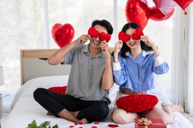 Couple in love holding red heart-shaped cards and smiling happy in Valentine's Day concept.