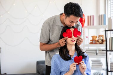 Couple in love holding red heart-shaped cards and smiling happy in Valentine's Day concept.