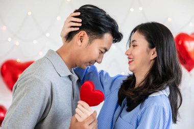 Couple in love holding red heart-shaped cards and smiling happy in Valentine's Day concept.