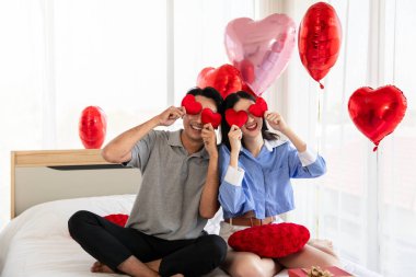 Couple in love holding red heart-shaped cards and smiling happy in Valentine's Day concept.