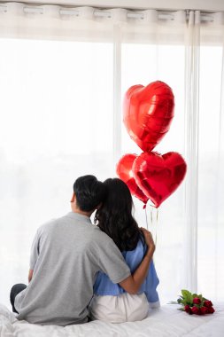 Back view of couple sitting on the bed, couple with red heart shape balloons Valentine's Day  concept.