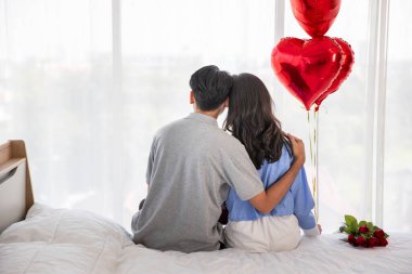 Back view of couple sitting on the bed, couple with red heart shape balloons Valentine's Day  concept.