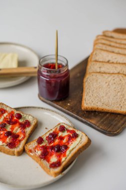 Bread with butter and cranberry jam is on the table and ready to eat. A delicious and sweet breakfast. Aesthetically pleasing serving of food. Recipe for toast with butter and jam. High quality photo