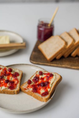 Bread with butter and cranberry jam is on the table and ready to eat. A delicious and sweet breakfast. Aesthetically pleasing serving of food. Recipe for toast with butter and jam. High quality photo