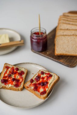 Bread with butter and cranberry jam is on the table and ready to eat. A delicious and sweet breakfast. Aesthetically pleasing serving of food. Recipe for toast with butter and jam. High quality photo
