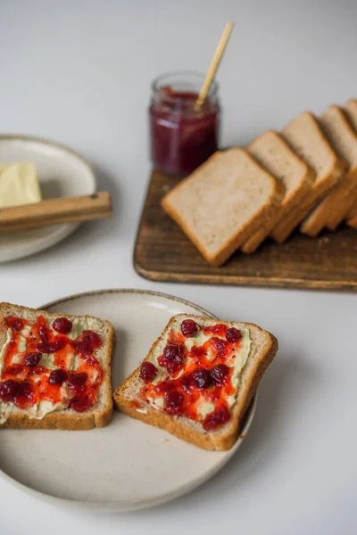 Bread with butter and cranberry jam is on the table and ready to eat. A delicious and sweet breakfast. Aesthetically pleasing serving of food. Recipe for toast with butter and jam. High quality photo