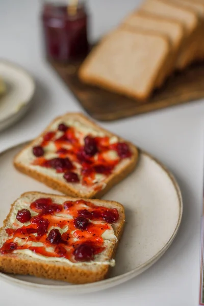Bread with butter and cranberry jam is on the table and ready to eat. A delicious and sweet breakfast. Aesthetically pleasing serving of food. Recipe for toast with butter and jam. High quality photo
