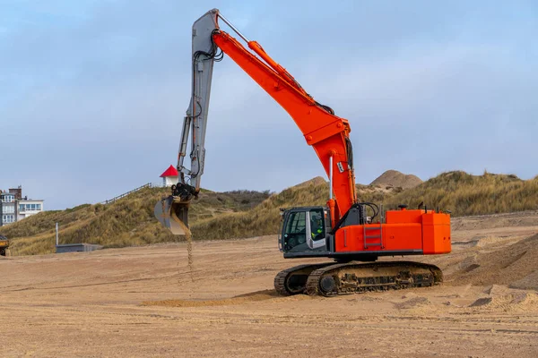 By the sea, an excavator is paving the sea sand .