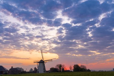Sabahın erken saatlerinde güneşin gökyüzünde doğduğu güzel bir yel değirmeni vardır.