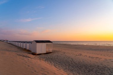 Deniz kenarında bir sıra plaj kulübesi var. Güneş batarken yan yana.