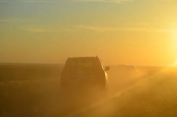 Cars in the dust on the road at sunset