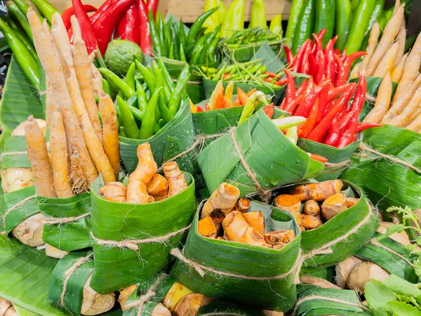 stock image Assortment of fresh peppers and roots, including red chilies, green chilies, turmeric, and ginger, wrapped in banana leaves at a market