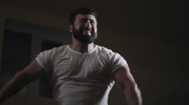 Atletik gücün düşük açılı görüntüsü. Güçlü beyaz adam spor salonunda gücünü ve kaslarını dramatik ışıklandırmayla gösteriyor. Spor salonunda güçlü bir adamı vurmak..