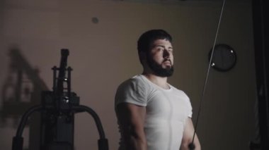 Güçlü beyaz adam triseps kaslarını çalıştırıyor spor salonunda dramatik ışıklandırmayla kablo çekiyor. Spor salonunda güçlü bir adamı vurmak..