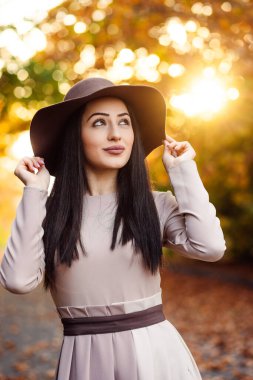 Sonbaharın güzelliğini keşfetmek. Altın sonbahar manzarasına karşı geniş kenarlı şapka takan zarif bir kadın.