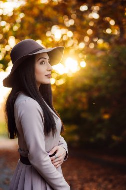 Havalı, şık bir kadın. Puslarla dolu bir parkta sonbahar günbatımının tadını çıkarıyor..