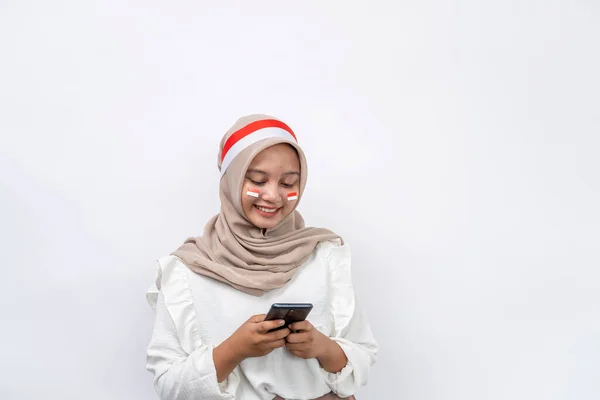 彼女のスマートフォンを見ている陽気なアジアの女性は 白い背景で孤立したインドネシアの独立記念日を祝います 8月17日のインドネシア独立記念日 — ストック写真